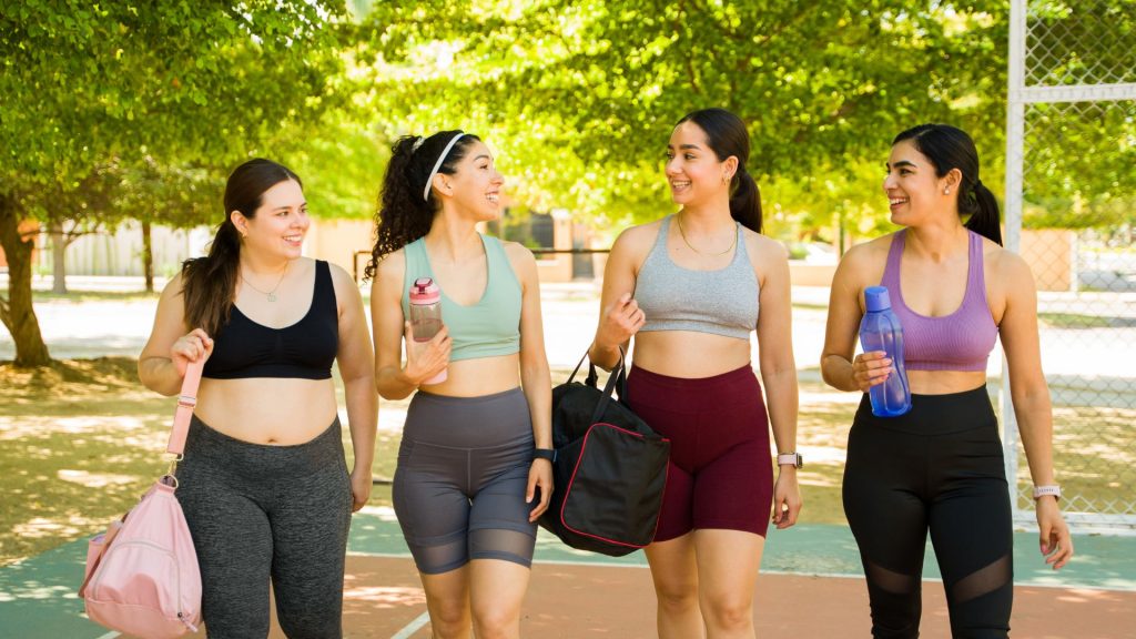 A group of four friends in workout clothes walk and talk in a park.
